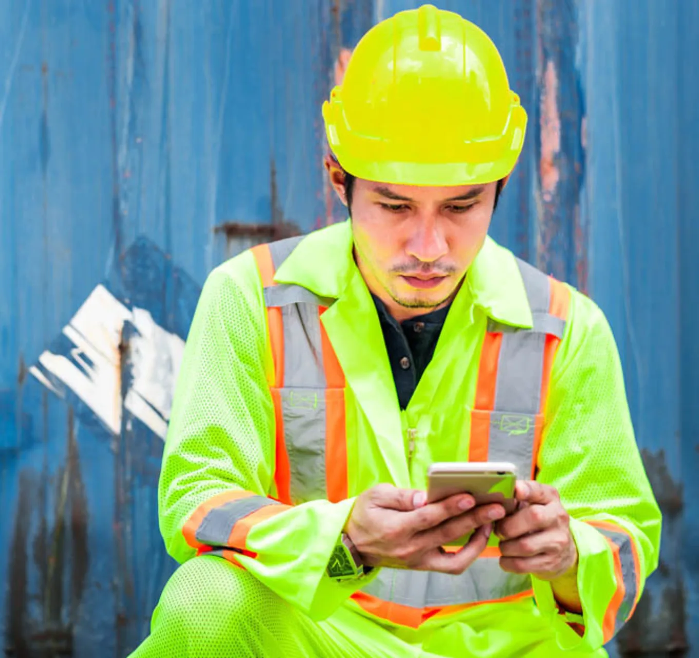 A worker wearing full personal protective equipment uses his cell phone.