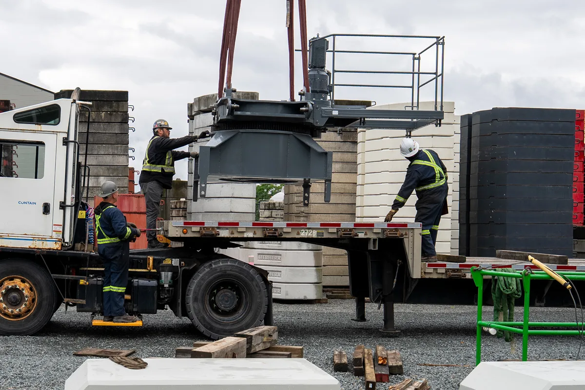 A crane operator oversees a lift and lowers a load while two other workers assist.