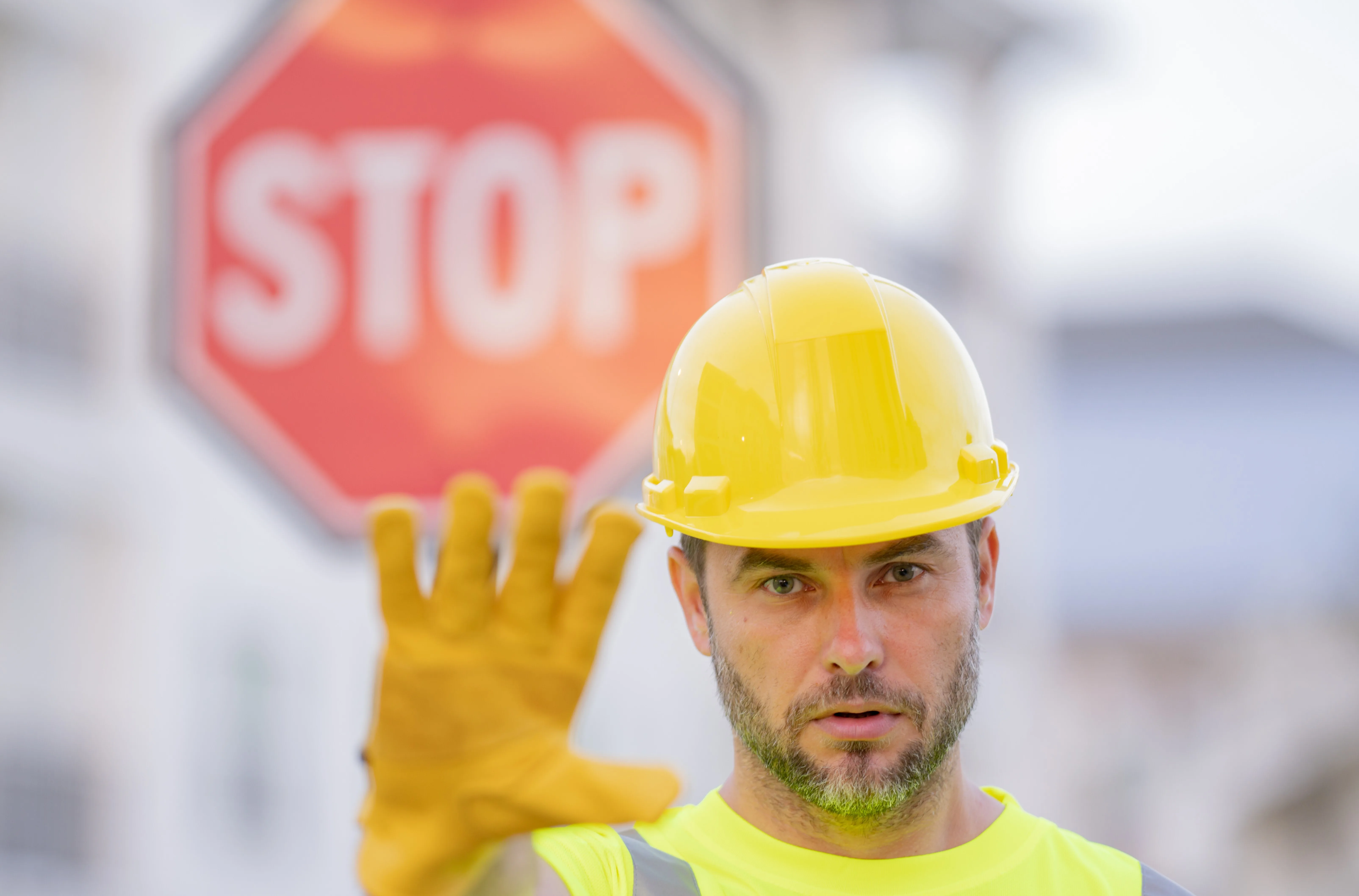 Worker holding hand up with stop sign in background.