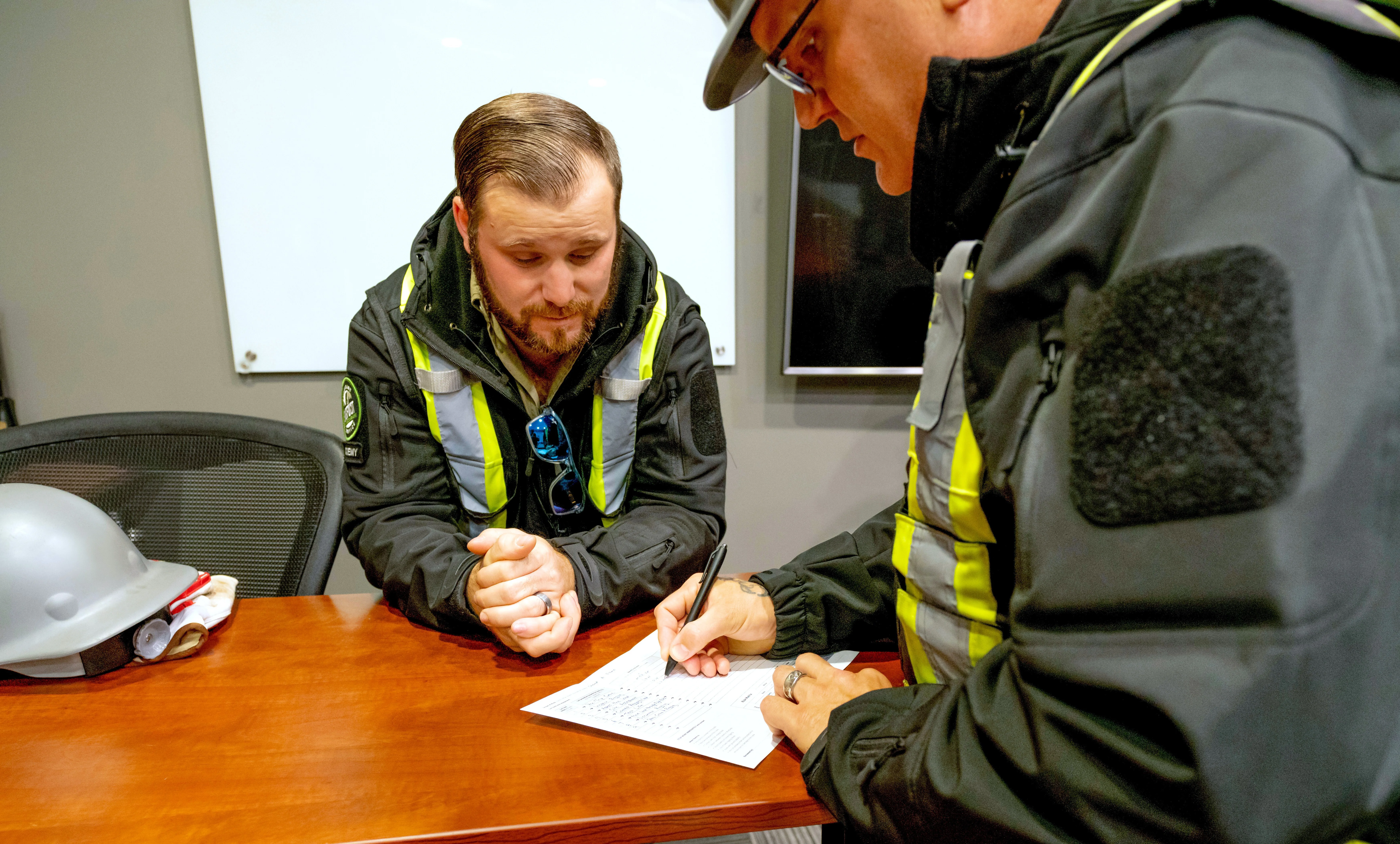 Two workers at a desk filling out a Field Level Hazard Assessment (FLHA) form.