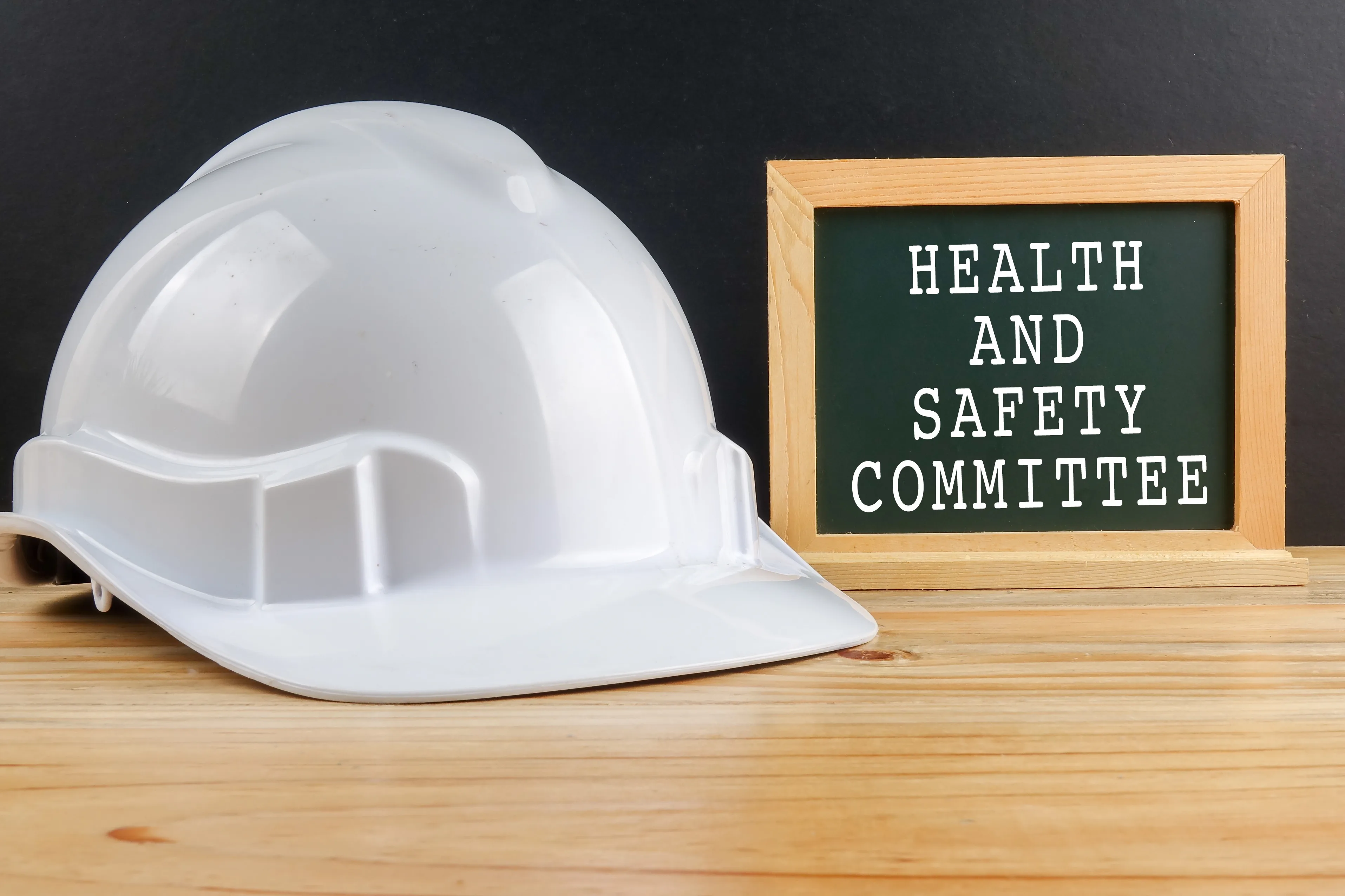 A white hard hat and joint health and safety committee sign is on a birch coloured table.
