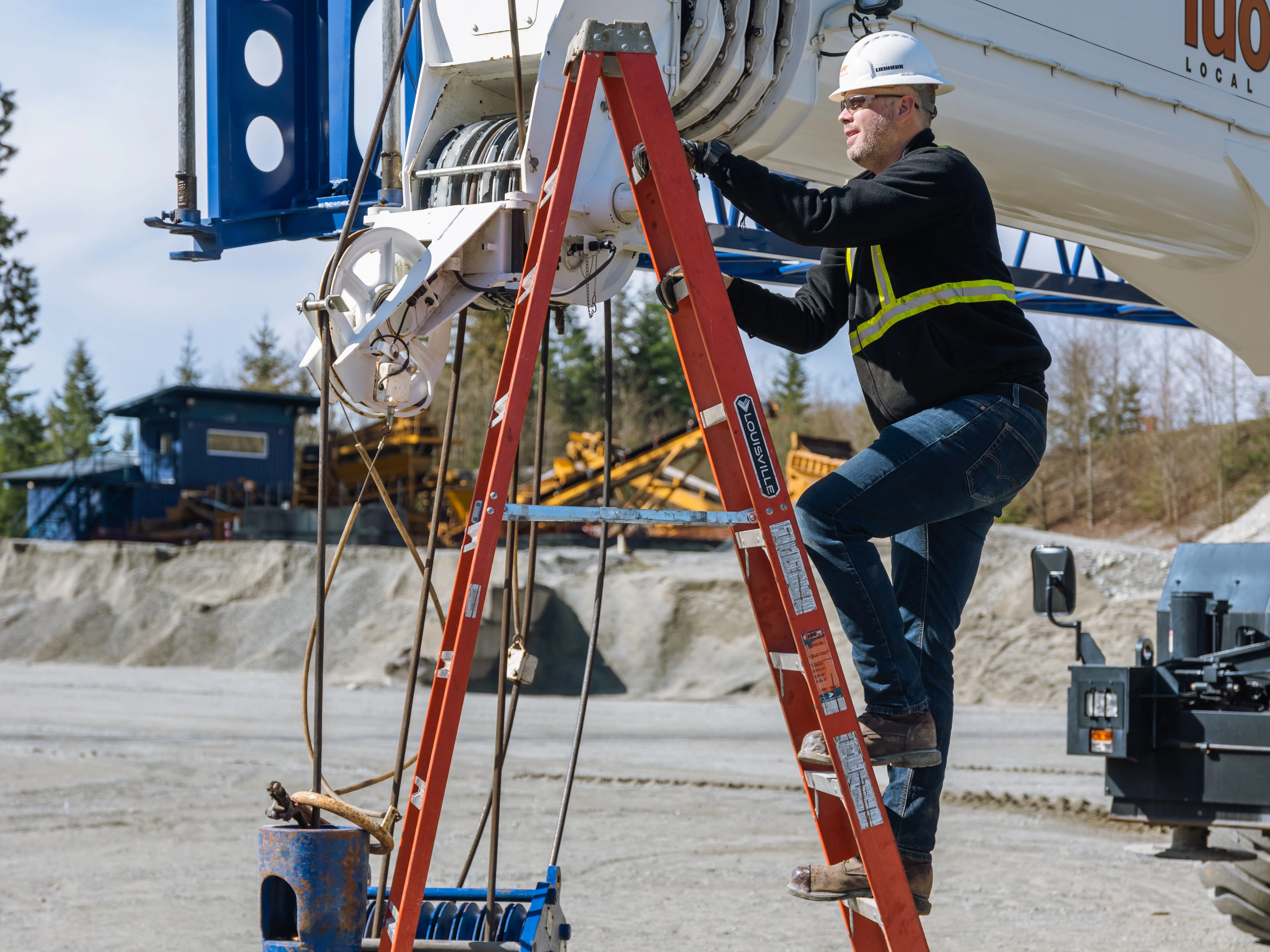 A man wearing personal protective equipment climbs a ladder to reach a mobile crane boom while maintaining three point contact.