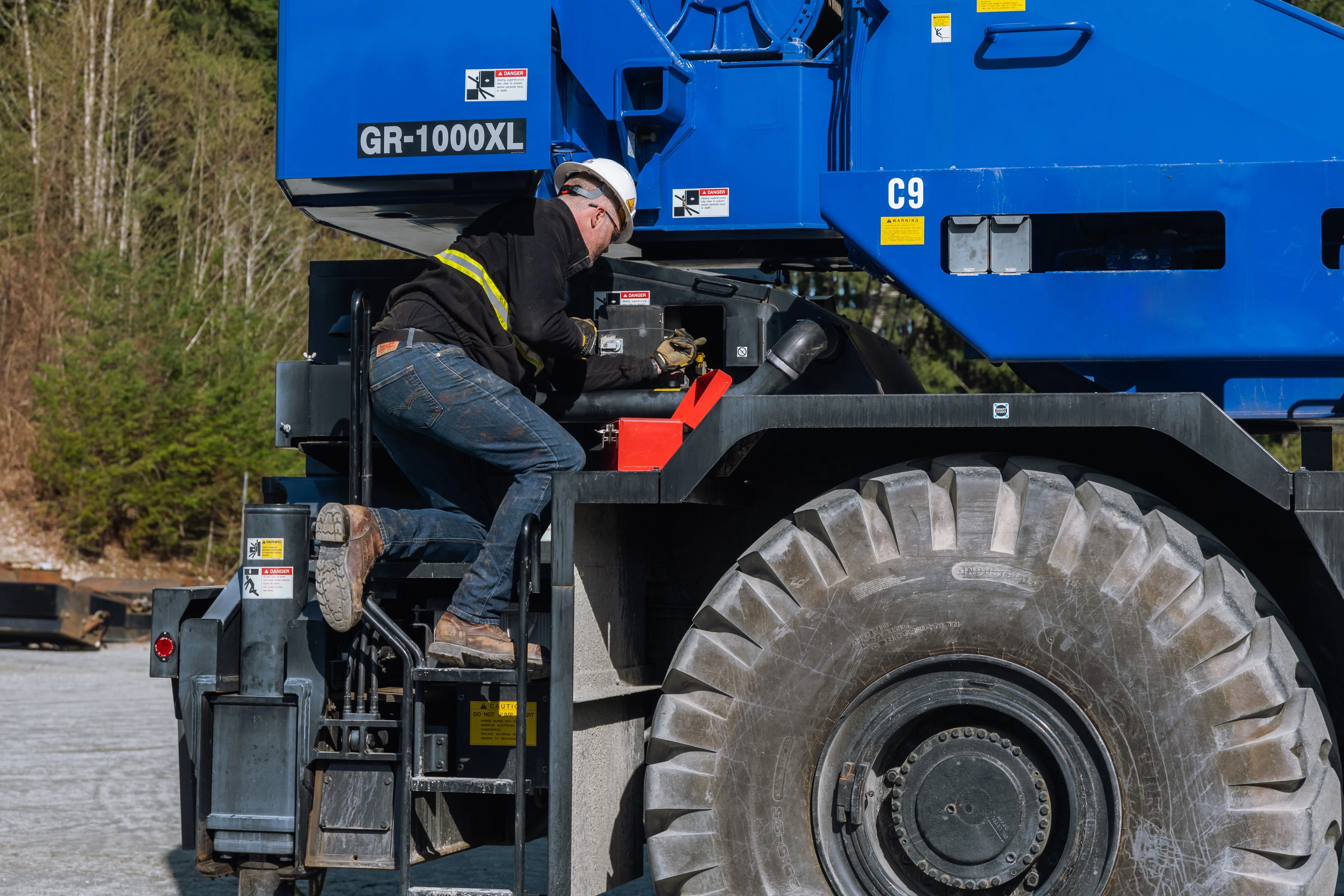 A worker performs maintenance on the side of a mobile crane whilte maintianing three point contact.