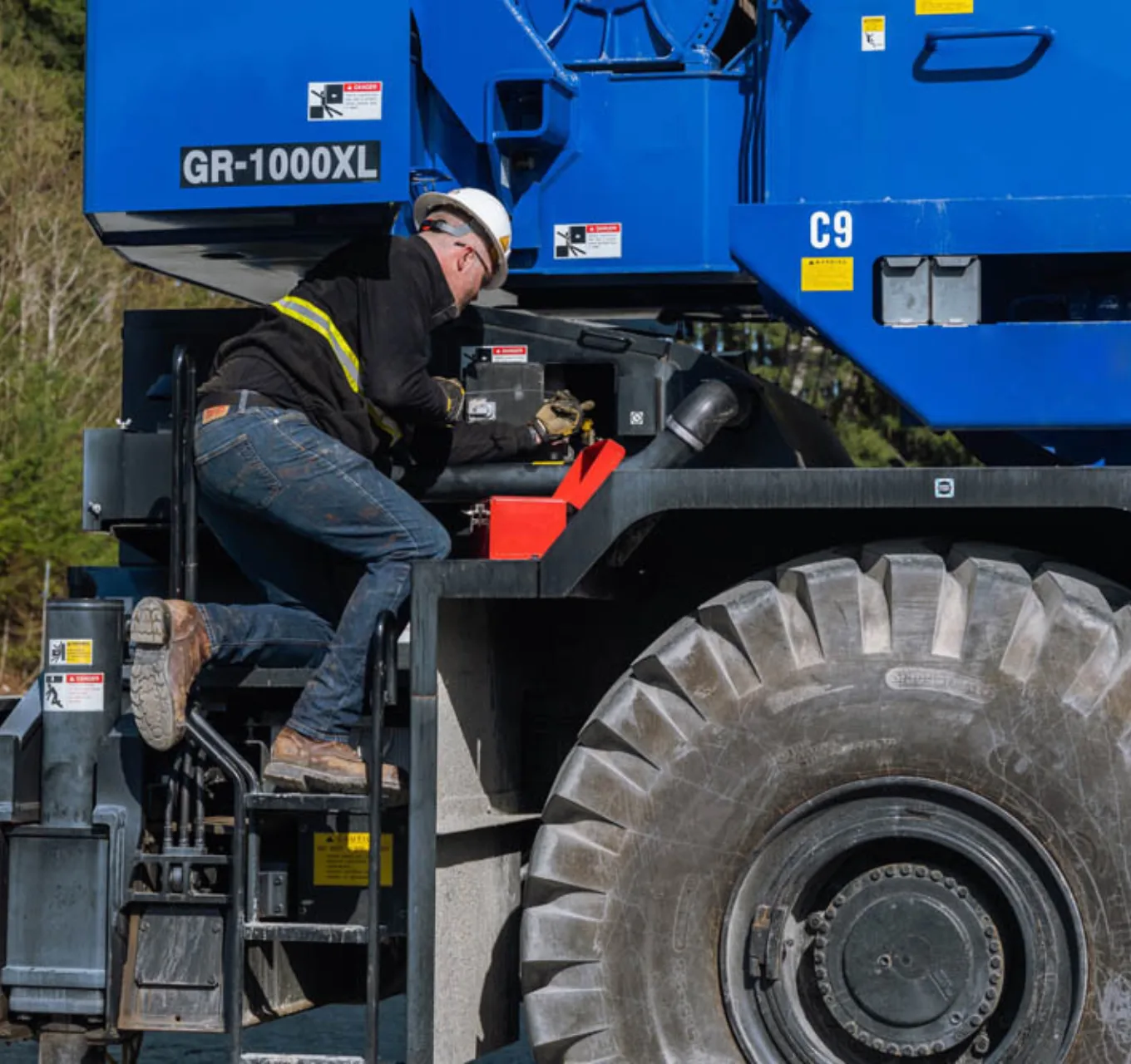 A worker performs maintenance on the side of a mobile crane whilte maintianing three point contact.