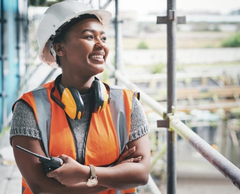 Woman who is black wearing a safety vest and hard hat working as a crane operator