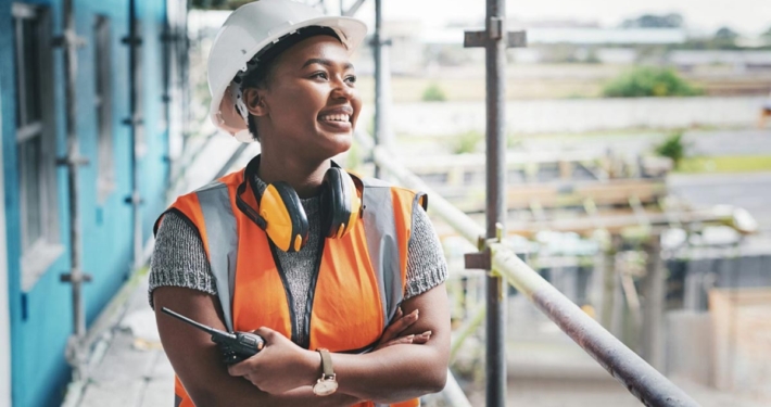 Woman who is black wearing a safety vest and hard hat working as a crane operator